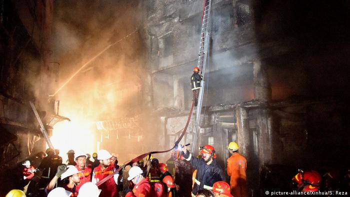 Firefighters climb a ladder leading against a charred building