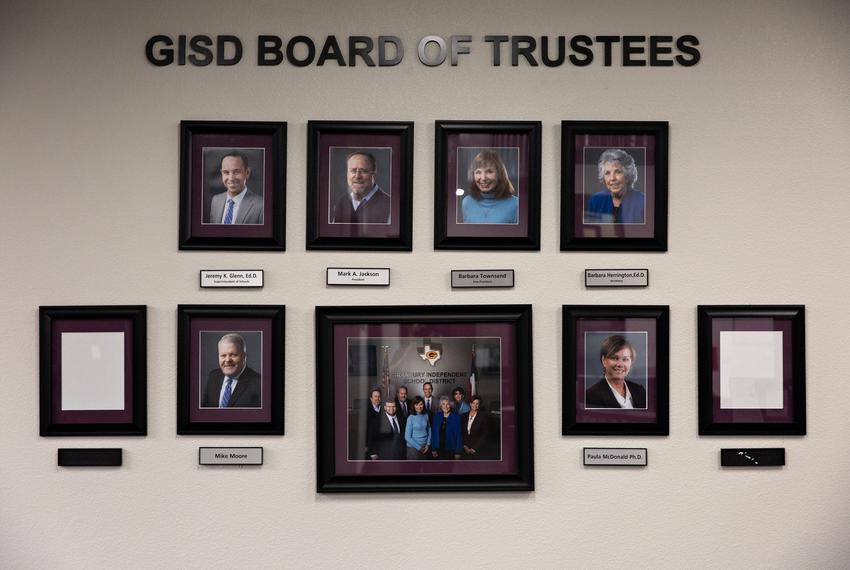 Two empty frames hang along with the portraits of the Granbury ISD Board of Trustees prior to the election of two new board …