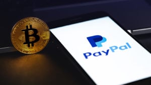Image of the PayPal logo on a smartphone next to a physical bitcoin token.