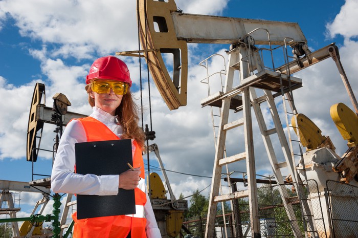 A person in protective gear in front of oil wells.