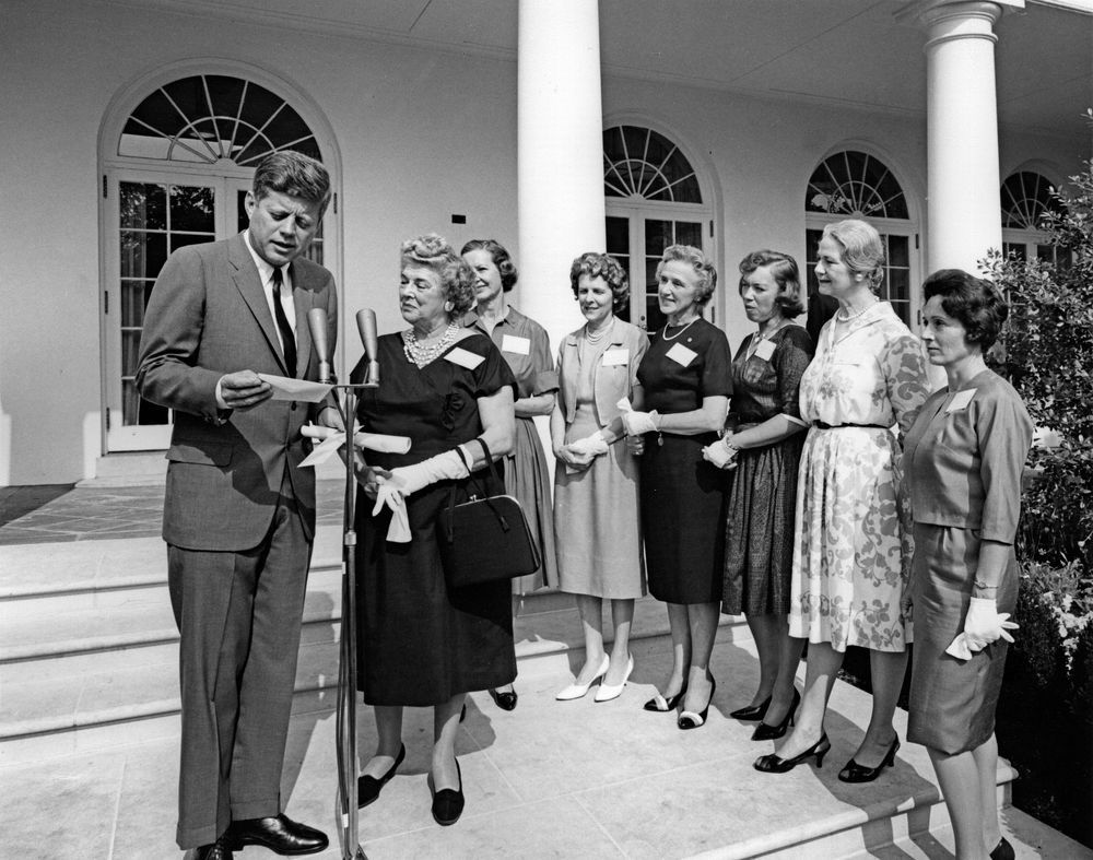 President John F. Kennedy delivers remarks to members of The Ninety-Nines, Inc., International Organization of Women Pilots, during a visit regarding the issuance of an Amelia Earhart commemorative stamp. Left to right: President Kennedy; past International President, Blanche Noyes; International President, Louise M. Smith; Virginia Thompson; Alice Hammond; Marion Andrews-Lopez; Fay Gillis Wells; unidentified. Rose Garden, White House, Washington, D.C. (Photo: Public domain)