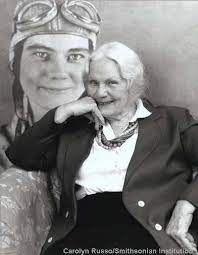 Fay Gillis Wells with a photo of her from an earlier time in the background. (Photo: Carolyn Russo/Smithsonian Institution)
