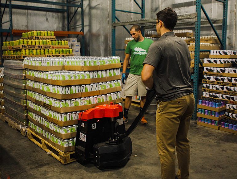 Employees at Artisan Beverages move a pallet of can beverages