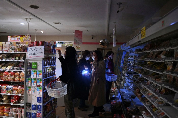 People shop in a darkened store during a power cut caused by an earthquake in Tokyo on March 16