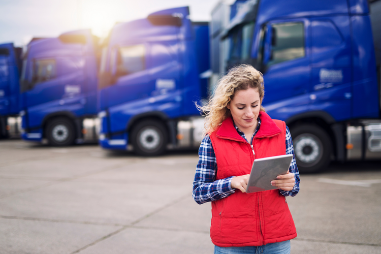 Women checking tablet in front of line of trucks