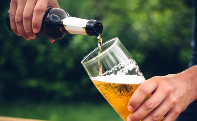 Man's hands pouring a glass of beer in a back yard with a plate of spicy chicken wings on the wooden table in the foreground