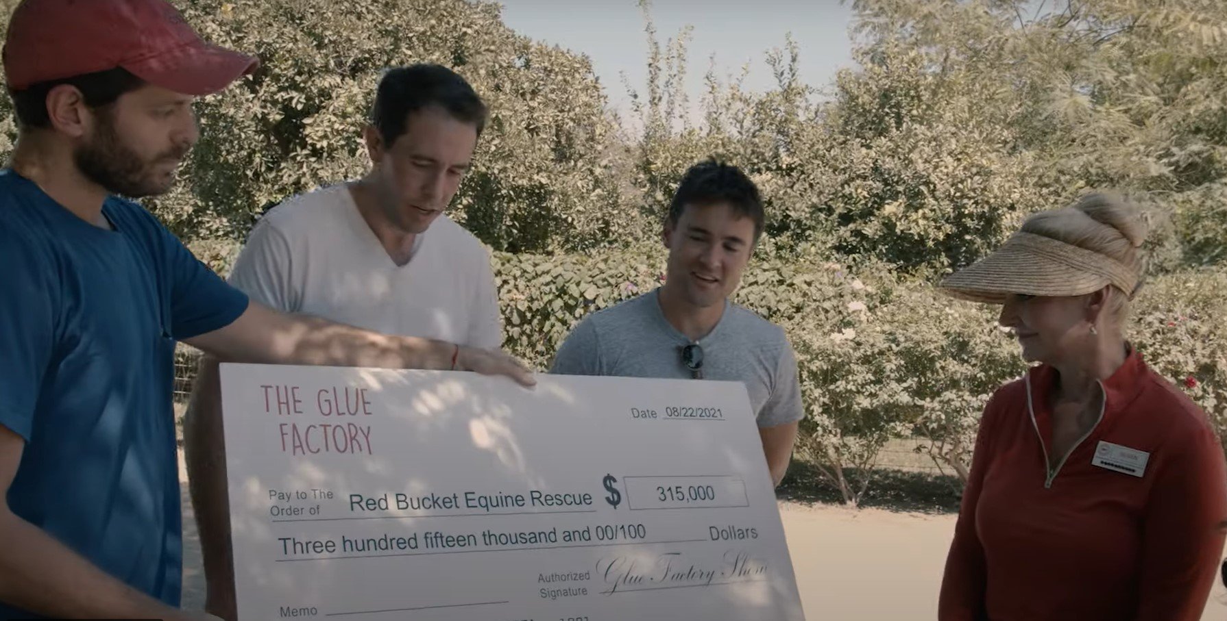 three men presenting a woman with a large check