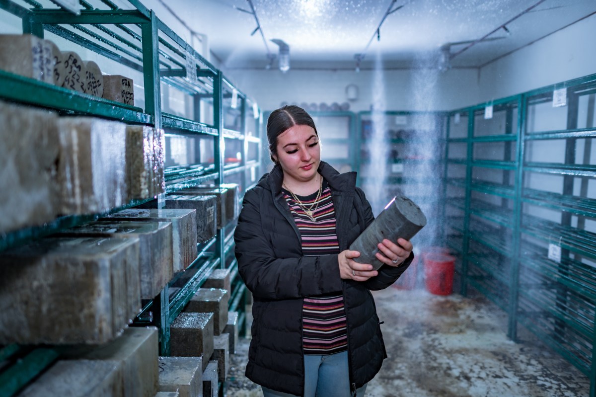 Casey Cowern stands in the curing room examining one of her concrete cylinders as mist rains above her.