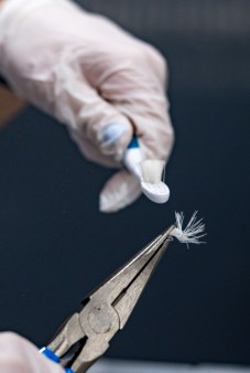 Needle-nose pliers hold a clump of toothbrush bristles while a nearby hand holds out a toothbrush they were plucked from.