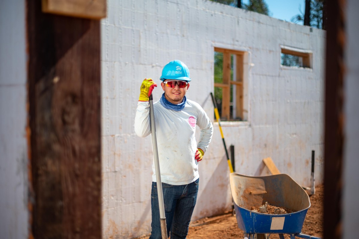 Moises Mendoza stands among the walls of a concrete-insulated-form home next to a wheelbarrow of soil with a shovel in hand.