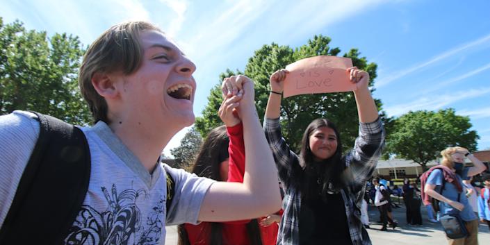 A high school student raises their fist while another holds a sign that says "Love is Love."