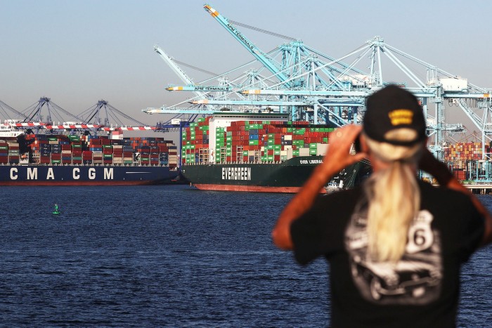A person rides aboard a ferry near shipping containers stacked on container ships at the Port of Los Angeles