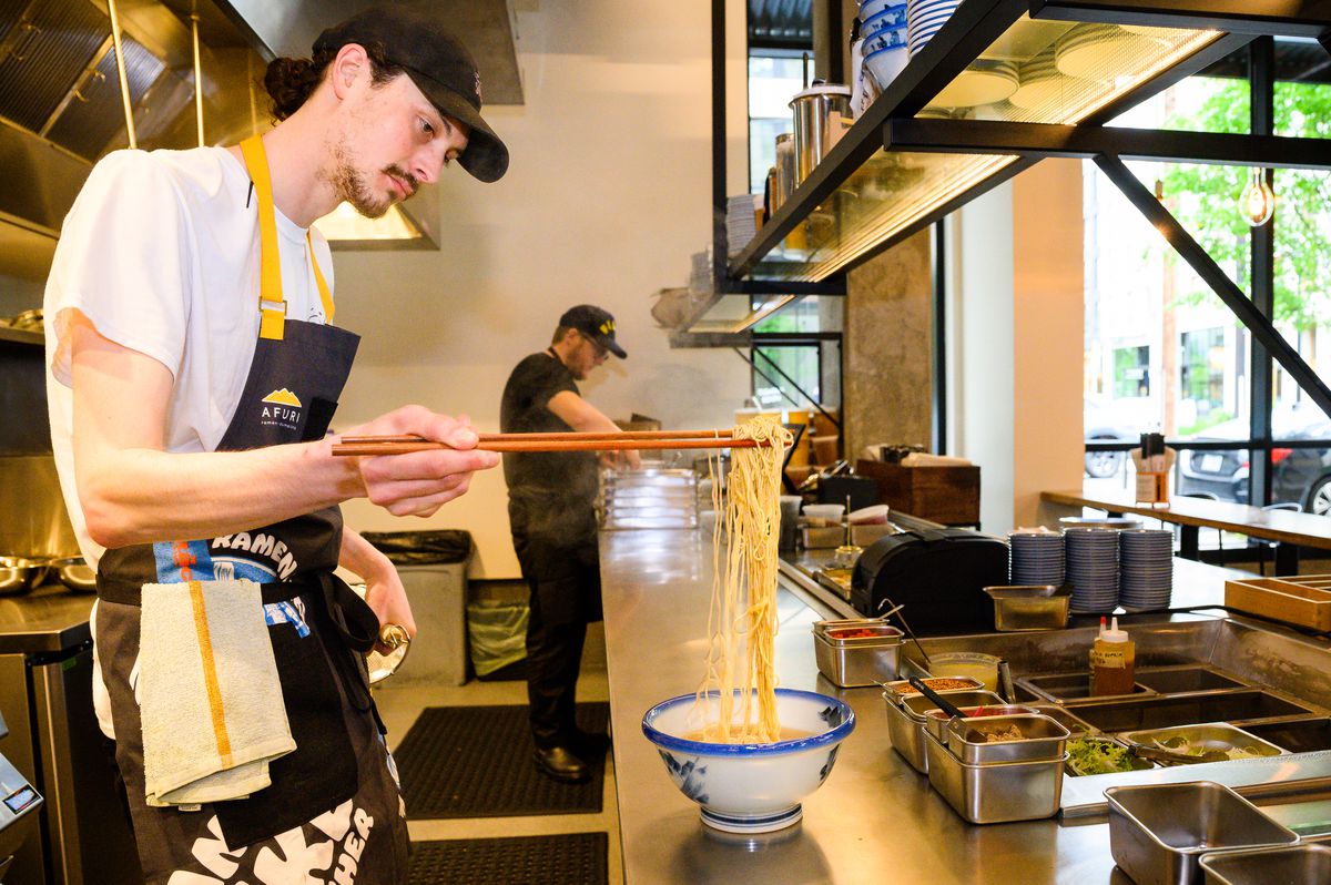 A man in an Afuri apron holds up ramen noodles over a bowl.
