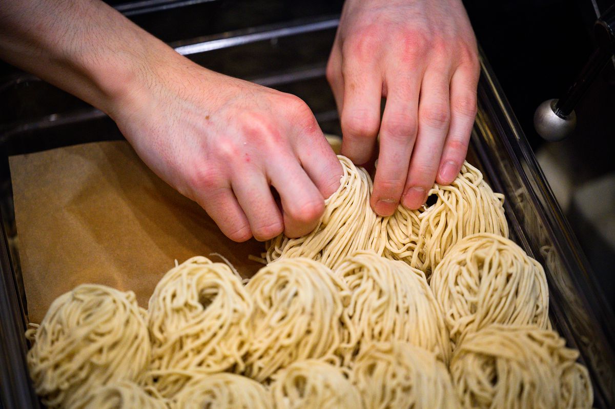 Two hands pinch nests of white noodles at Afuri.