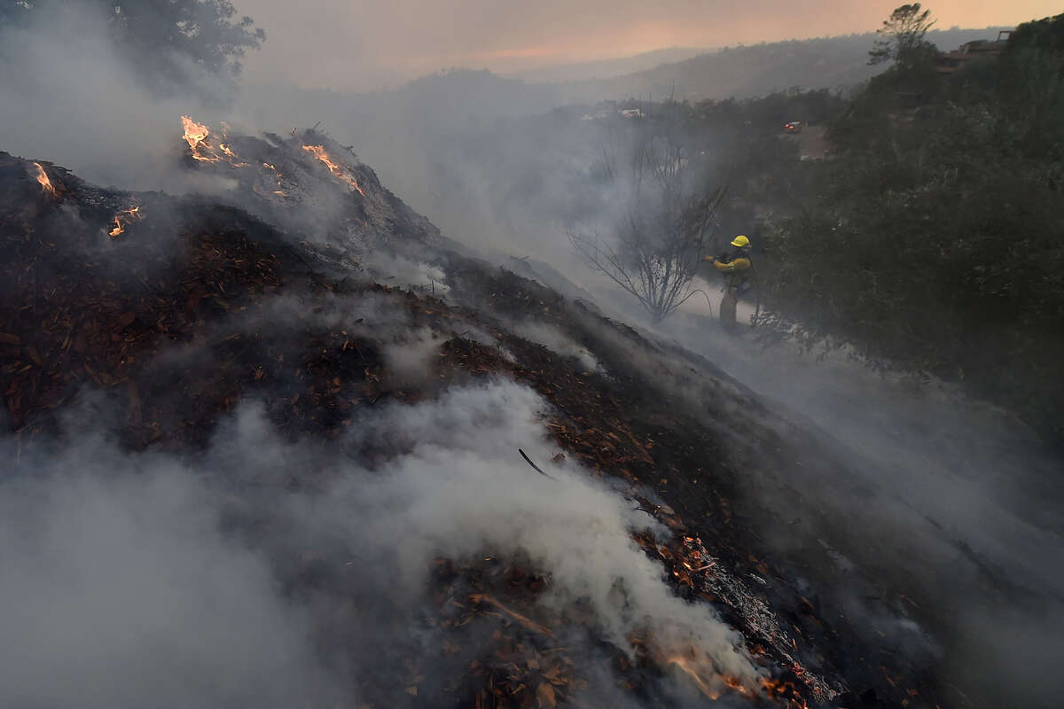 A firefighter puts out hotspots on a smoldering hillside in Montecito as strong winds blow smoke and embers inland, Dec. 16, 2017, at the Thomas Fire.