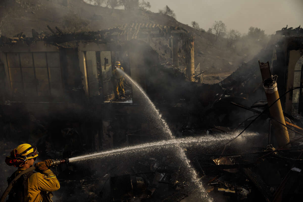 Humboldt County firefighters Lonnie Risling, left, and Jimmy McHaffie, right, spray down smoldering fire underneath the rubble of a home that was destroyed by the Thomas Fire, on Dec. 17, 2017, in Montecito.