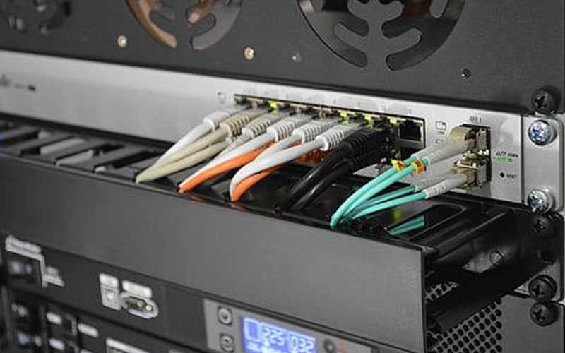 Image of a server IDF with network cables inserted in the switches and a blurred digital display panel underneath with numbers 225 and 032 displayed.