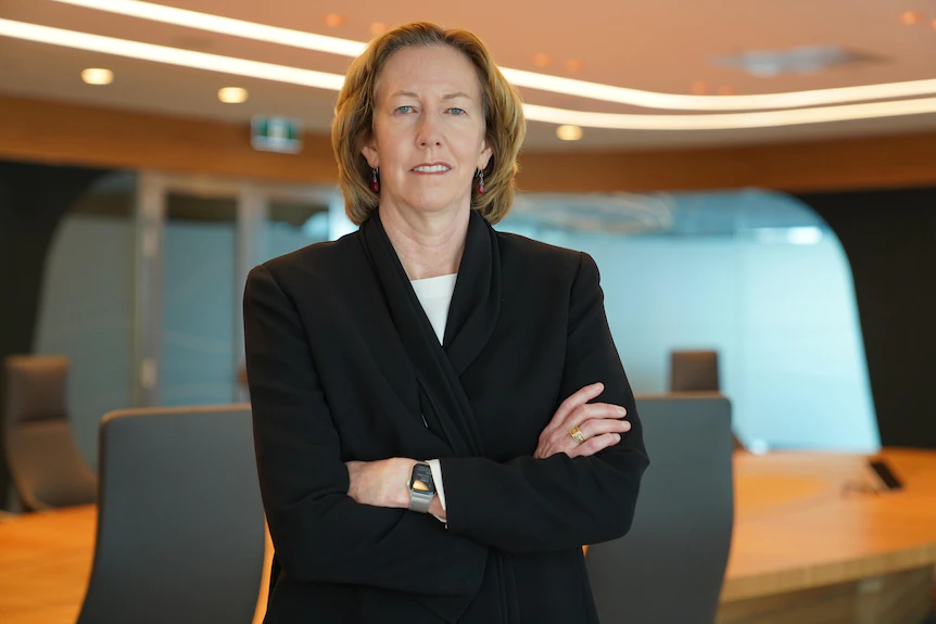 Woman wearing a suit with her arms folded standing in a conference room.