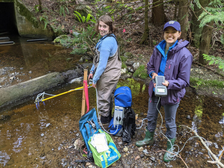two researchers sample water in a stream.