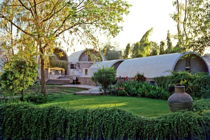 A series of low buildings with curved roofs sit in landscaped surroundings