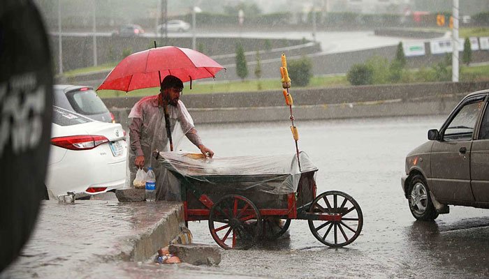 A vendor is covering himself with an umbrella and his cart with a plastic sheet during in Rawalpindi on July 1, 2022. Photo: APP