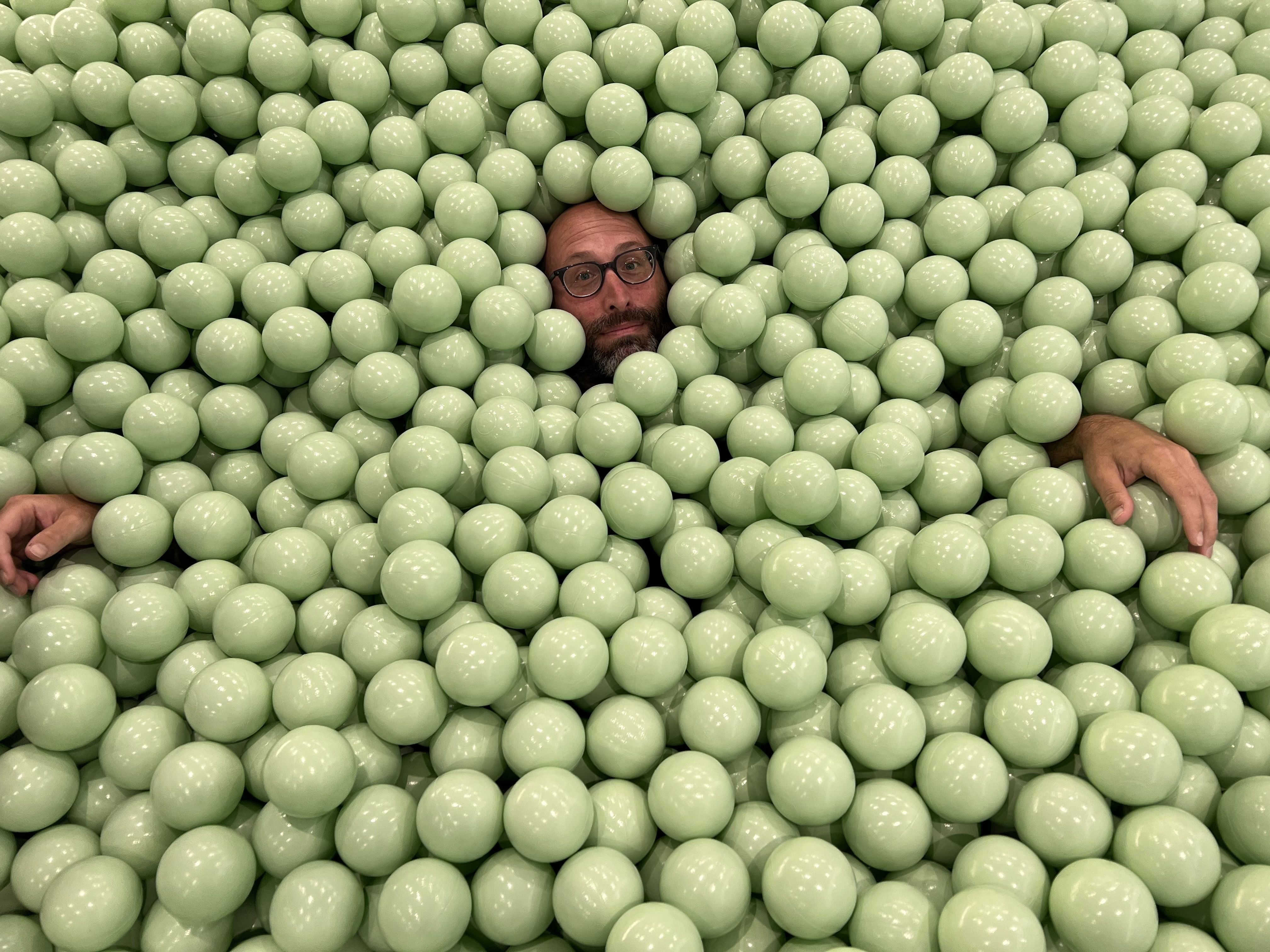 Photo of a man submerged in plastic balls in a ballpit.