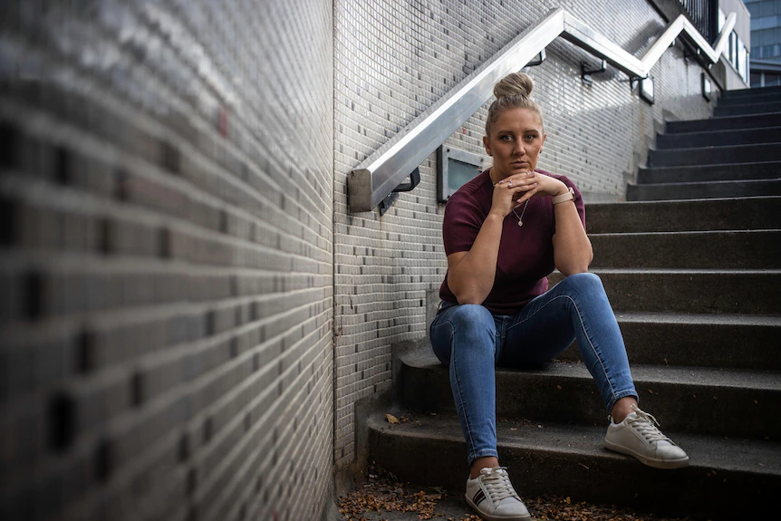Woman in jeans, maroon top and white sneakers sitting down on stairs.