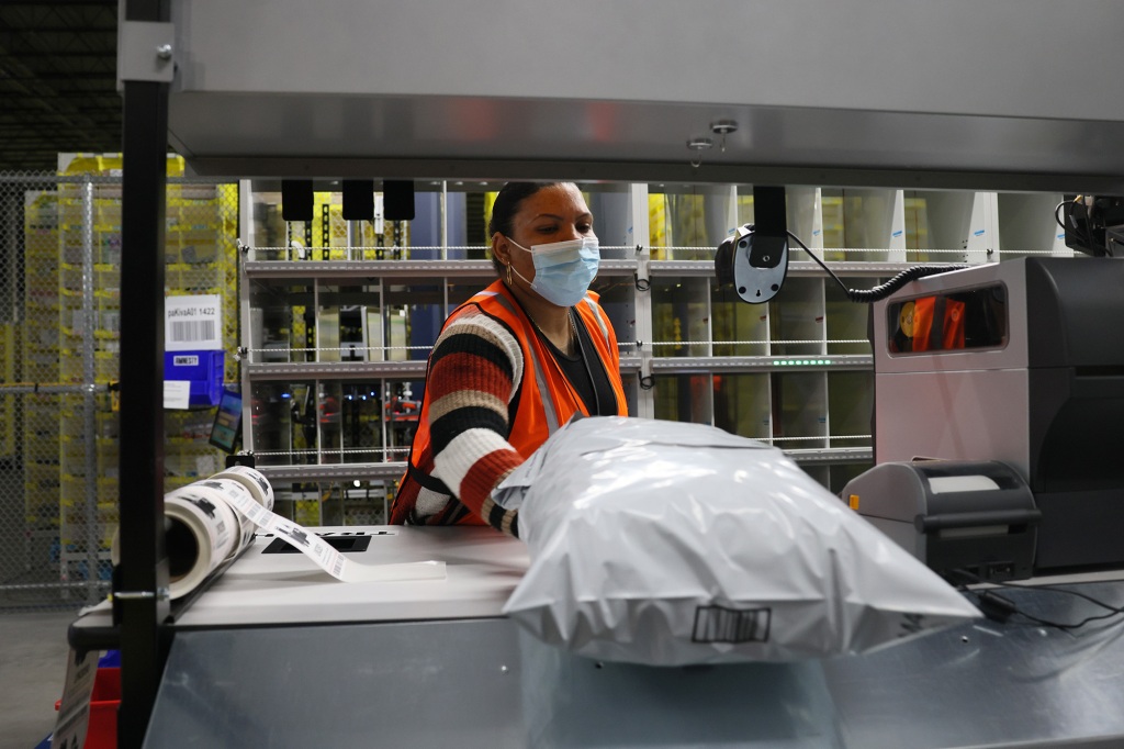 An Amazon worker with a package in a plastic wrapping.