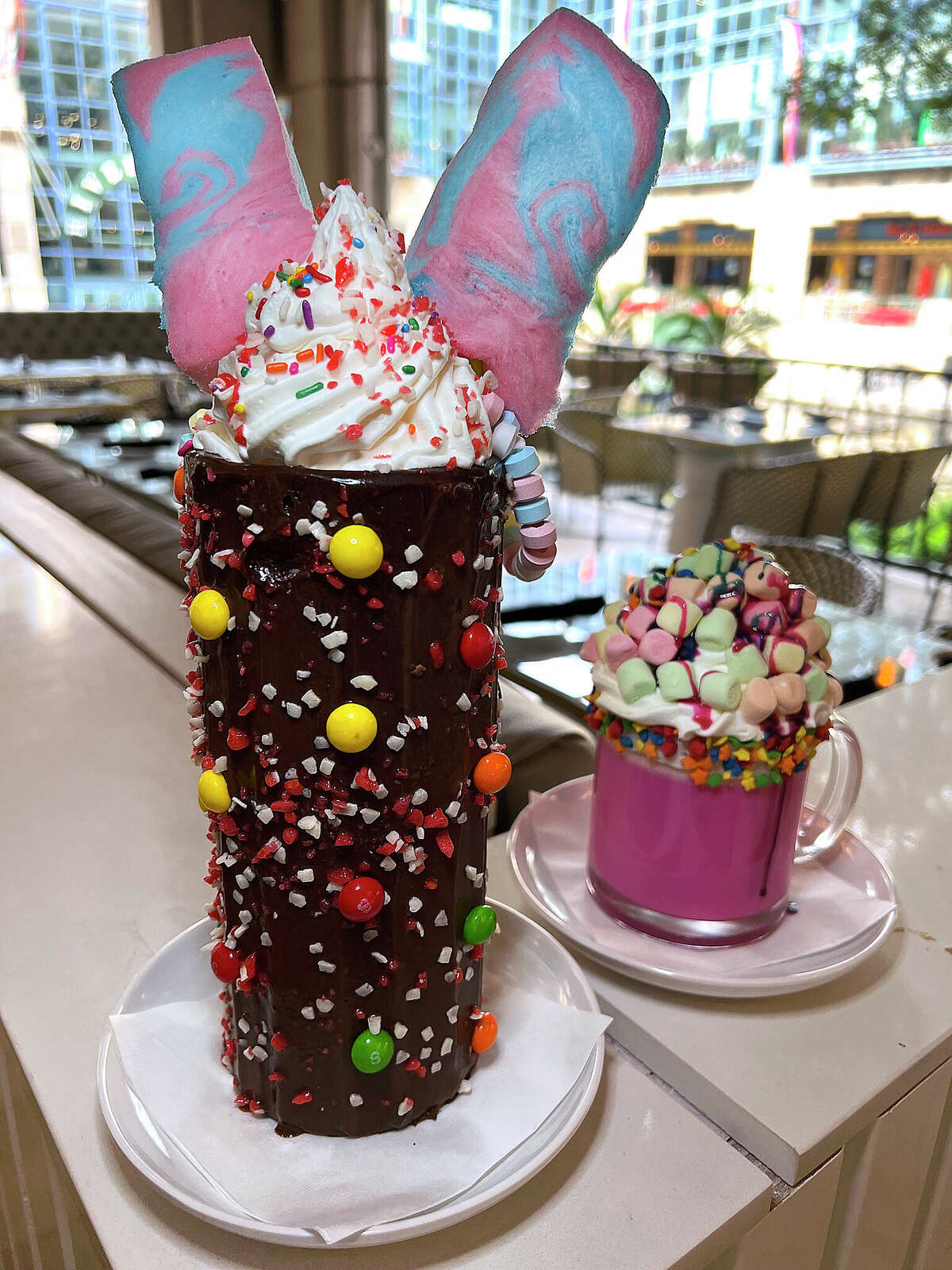 The Tie Dye milkshake, left, includes vanilla ice cream, vanilla sauce, cotton candy, candy necklaces and a glass coated with chocolate, Skittles and Pop Rocks at Sugar Factory American Brasserie at The Shops at Rivercenter on the San Antonio River Walk. Pink Unicorn Hot Chocolate is made with white chocolate, whipped cream and marshmallows.