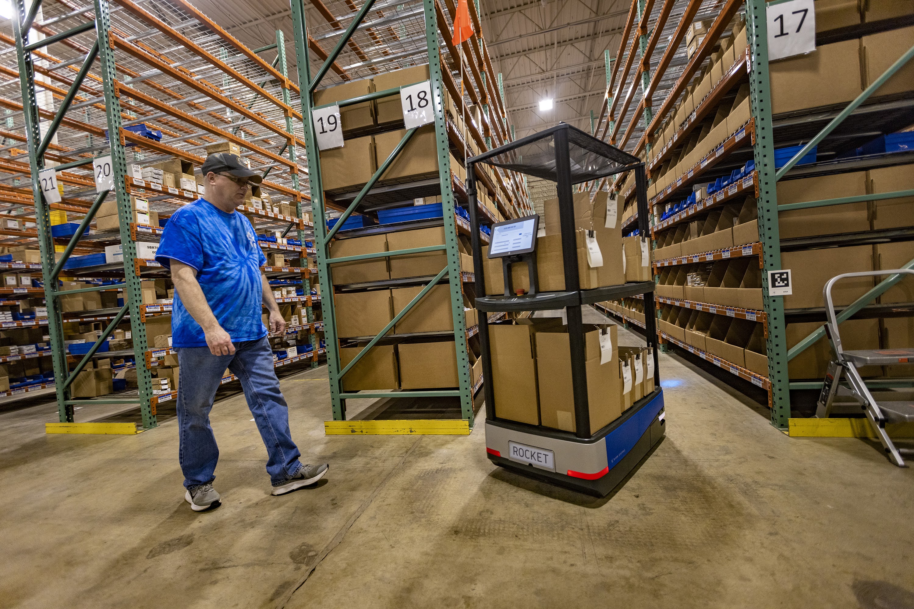 Distribution associate Joseph Montville follows Rocket, a robotic “Chuck,” as it turns into an aisle at the Top Notch Distributors warehouse fulfilling a customer order. (Jesse Costa/WBUR)