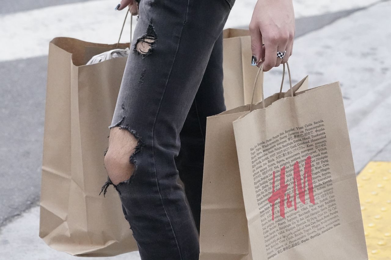A person in torn jeans carries bags from the retailer H&M