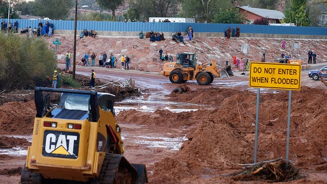 On lookers watch as construction equipment removes flood debris from Short Creek as it crosses Central Street on September 15, 2015 in Colorado City, Arizona. Flash Floods from heavy rains on the afternoon of September 14, 2015 washed away two cars in Hildale as they were crossing a flooded creek, killing 13 people.