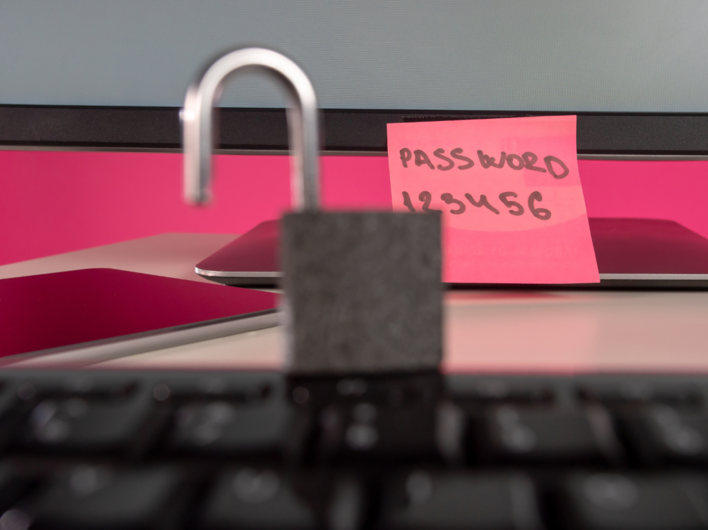 An image depicting poor password practices. It features a post-it with the words "PASSWORD" and "123456" written on it. It also features a padlock in the foreground.