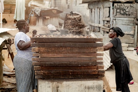 Women stacking trays over a fire as they prepare fish to be smoked