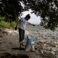 A volunteer picks up trash during a coastal cleanup drive at a protected bird sanctuary, in Paranaque City, Philippines. | REUTERS