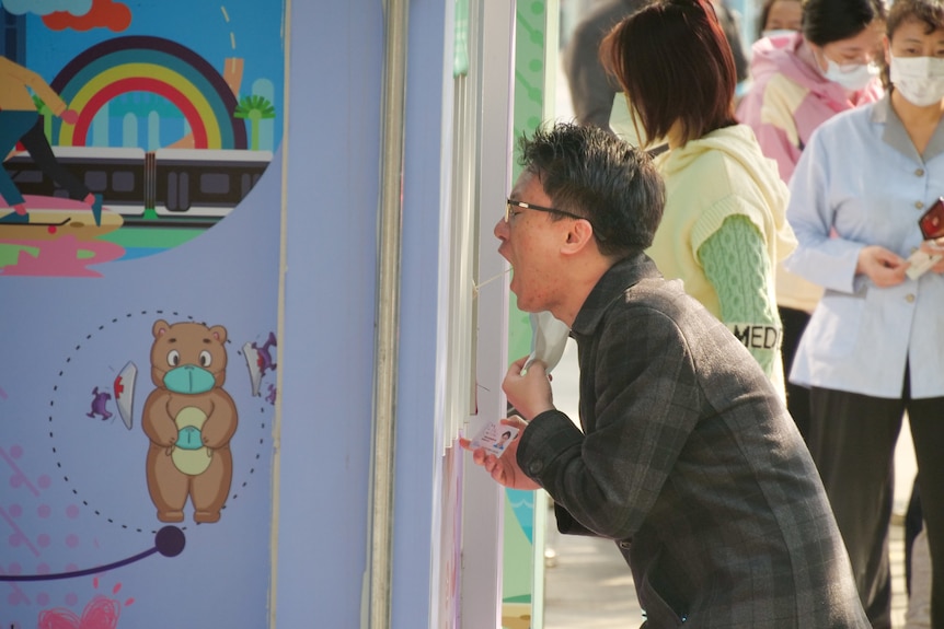 a man opens his mouth as an unseen figure sticks a swab down his throat